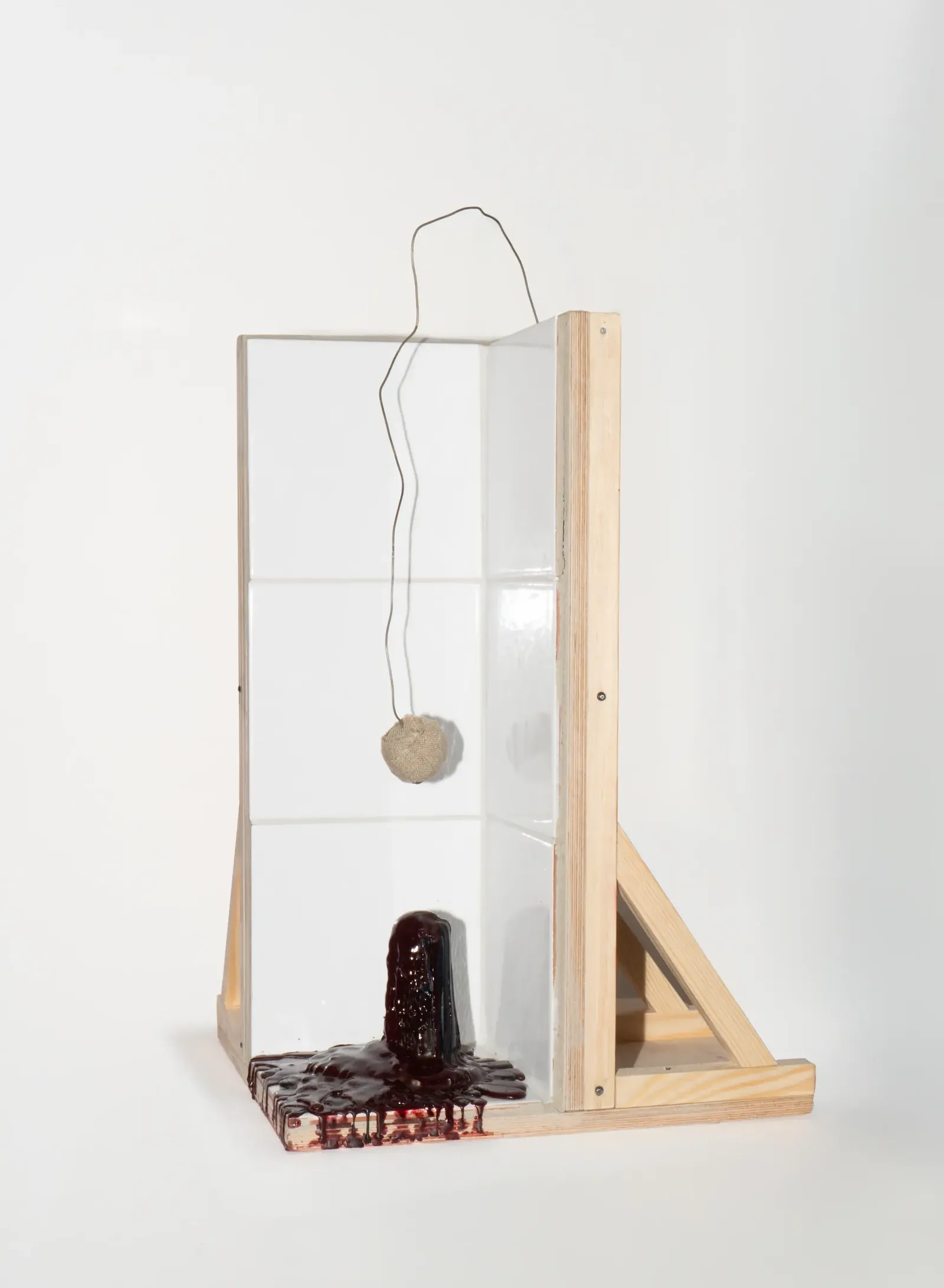 A plywood frame holding a thin wire from which a small clay weight hangs above a dark red base.