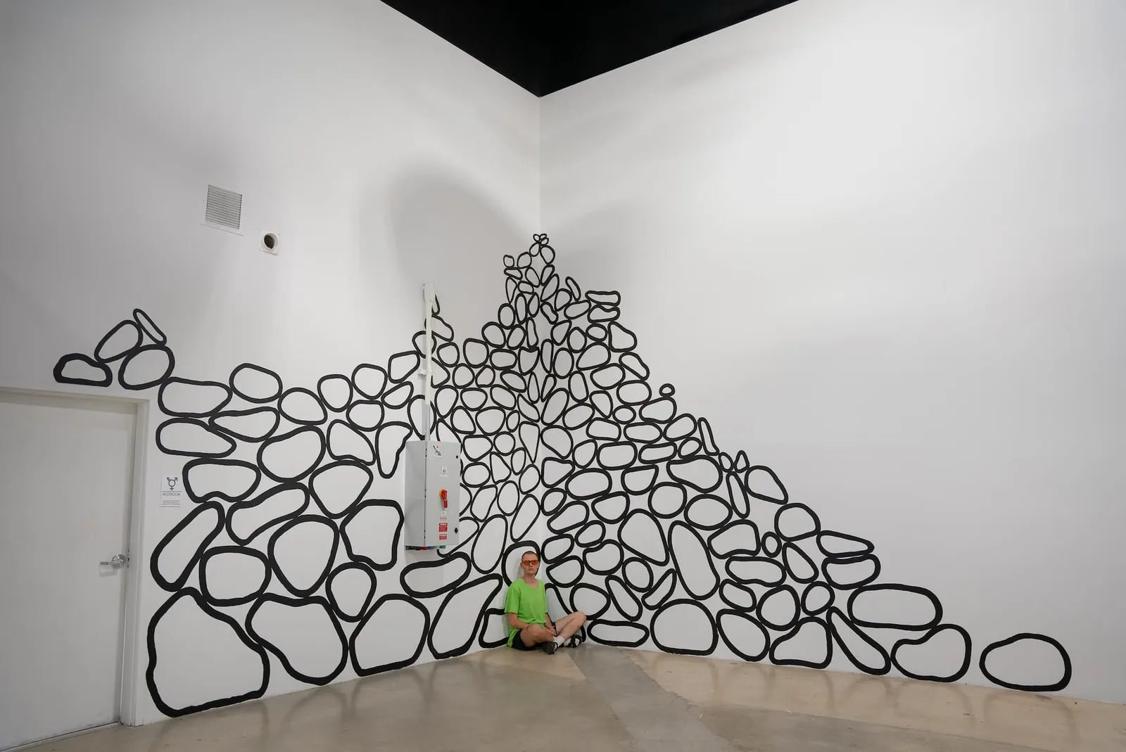 Black-outlined stones painted directly into the corner of a white gallery, piled as if just settled.