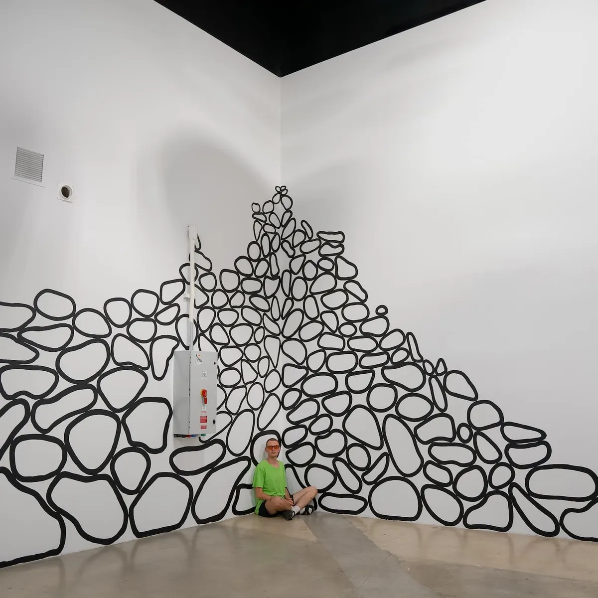 Black-outlined stones painted directly into the corner of a white gallery, piled as if just settled.