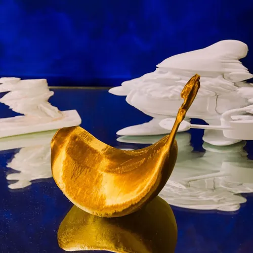 A golden distorted fruit form beside white 3D-printed shapes on a deep blue ground.