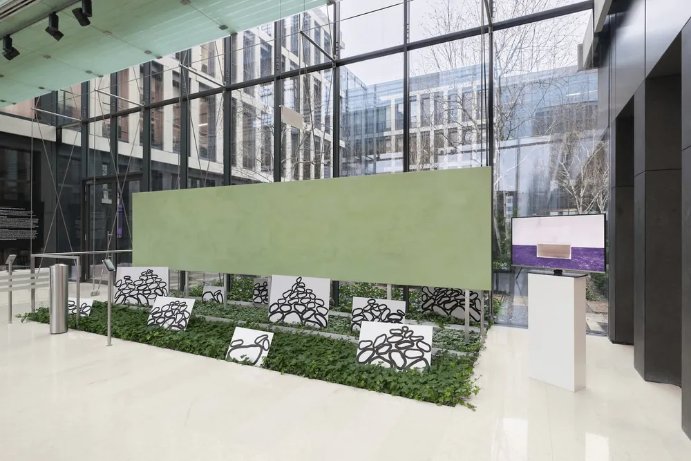 A long green painting hung above painted stone panels set in ivy, in a glass-walled lobby.
